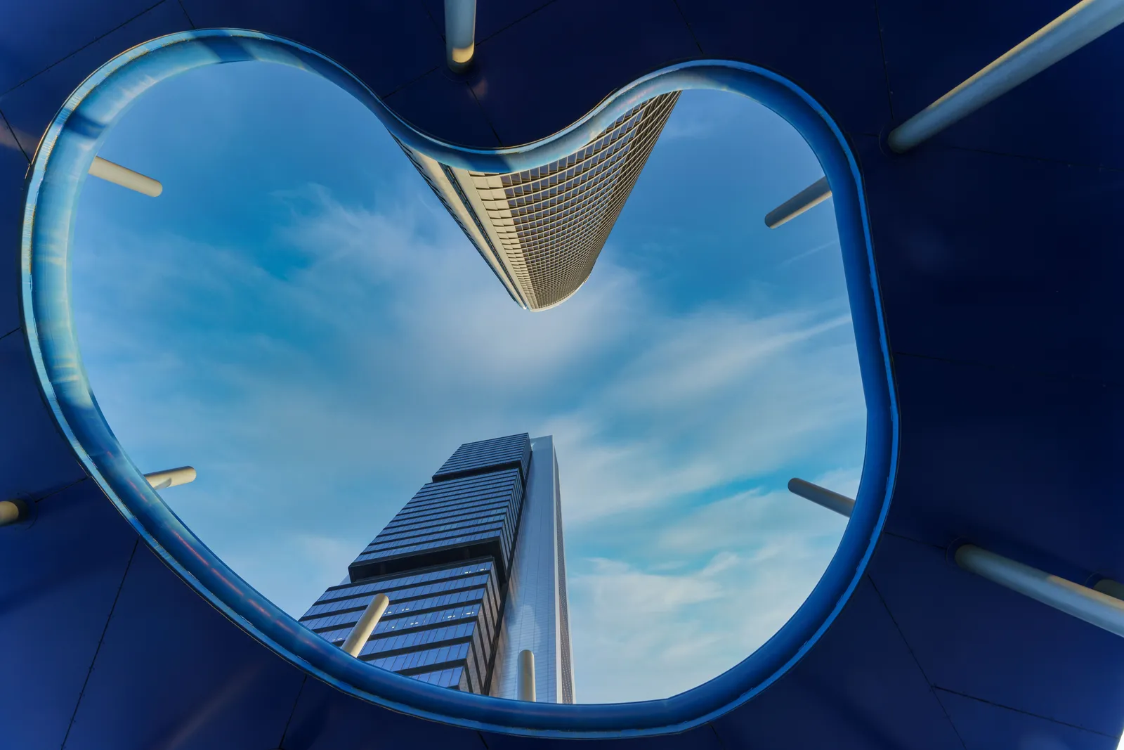 Looking up at two glass skyscrapers through a curved blue frame
